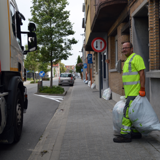 Huisvuilwagen in de straat en ophaler staat klaar met twee zakken in de hand